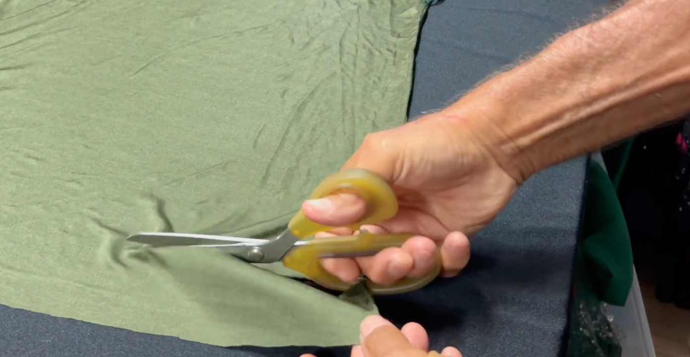 Tailor cutting green fabric with scissors during garment preparation at Doxa Couture in Downey, California.